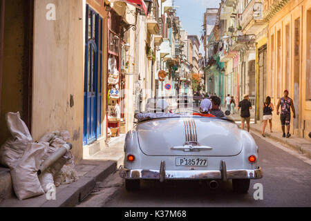 Scena di strada, i turisti navigare una stretta Habana Vieja strade in un bianco Pontiac classic car, Havana Cuba Foto Stock