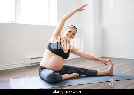 Donna incinta facendo stretching e yoga a casa Foto Stock