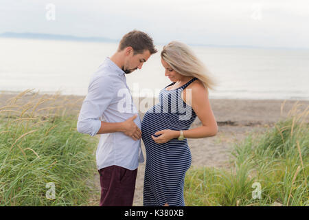 Donna incinta in spiaggia con il marito divertendosi Foto Stock