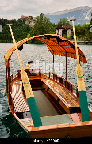 Tradizionale realizzato a mano in legno barca Pletna è dipinta con i remi e tettoia sul lago di Bled con il castello di Bled e Vila Preseren Slovenia Foto Stock