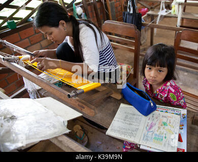 La madre lavora telaio mentre il bambino fa compiti a Siem Reap, Cambogia il Ott 11, 2011 Foto Stock