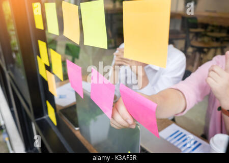 Uomo d'affari di incollaggio note adesive sulla parete di vetro in ufficio e discussting con il team. Foto Stock