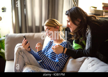 Persone relazioni. Due ragazze stanno parlando e utilizzando il cellulare sul divano Foto Stock