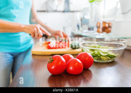 Donna matura in cucina prepara il pasto con i pomodori in primo piano Foto Stock
