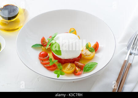 Antipasto italiano insalata caprese con maturi di rosso e di giallo di pomodori ciliegini, mozzarella, di foglie di basilico fresco e olio di oliva. Sfondo bianco. Foto Stock