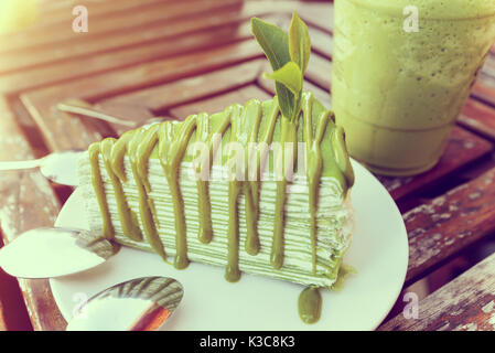 In stile vintage soft di foglia di tè ricamato sul matcha torta nella piastra bianca, posto in prossimità di un bicchiere di ghiaccio il tè verde su un vecchio tavolo di legno in serata sunli Foto Stock