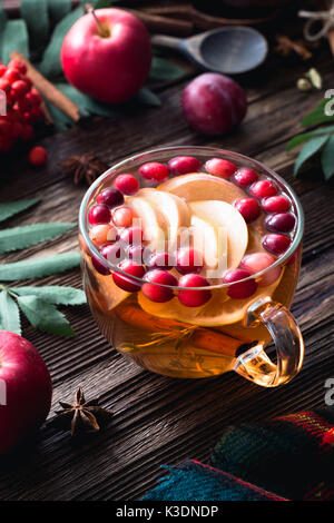 In inverno il riscaldamento berry tè con mirtilli rossi, Apple, cannella, limone, il miele e il timo in un bicchiere di vetro su un tavolo di legno. composizione verticale Foto Stock