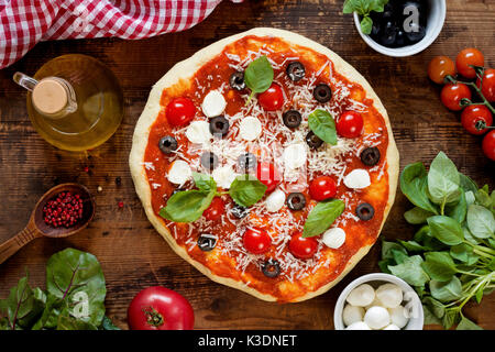 Hot pizza italiana con le olive, i pomodori, il basilico, il formaggio mozzarella. vista superiore Foto Stock