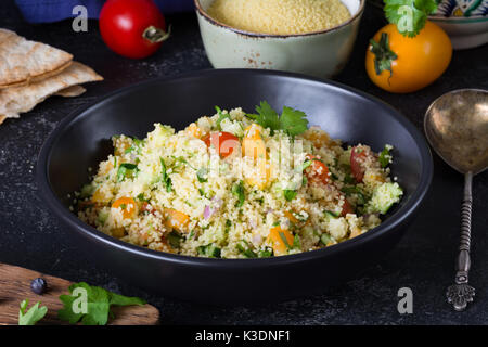 Arabo libanese cucina: una sana deliziosa insalata di cous cous, verdure fresche e verdi chiamato tabulé in nero ciotola. autentica cucina Foto Stock