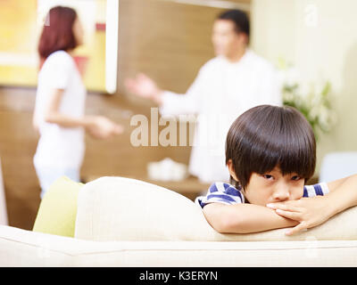 Bambino asiatico sembra triste e infelice mentre i genitori quarreling in background. Foto Stock