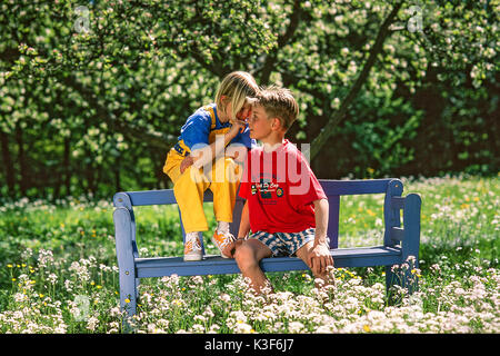 Ragazzo e una ragazza sedersi sulla panchina nel giardino e whisper Foto Stock