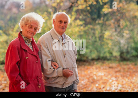 Senior Citizen's giovane passa per una passeggiata a braccetto in legno Foto Stock