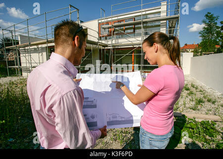Coppia giovane con un architetto ha il piano nella parte anteriore del guscio Foto Stock
