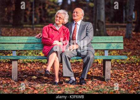 Senior Citizen's giovane siede insieme su una panca in legno in legno Foto Stock