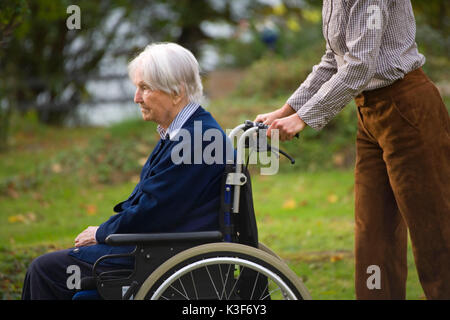 Senior è azionata in una sedia a rotelle Foto Stock