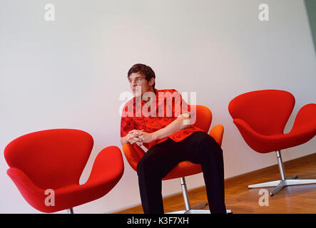 Giovane uomo si siede pensieroso / annoiato in poltrona orangem Foto Stock