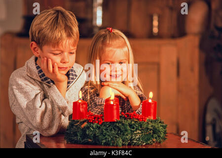 Due bambini mentre una corona di Avvento in cui tutte e quattro le candele bruciano Foto Stock