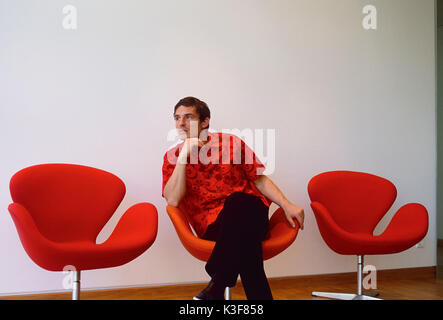 Giovane uomo si siede pensieroso / annoiato in poltrona orangem Foto Stock