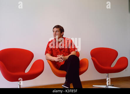 Giovane uomo si siede pensieroso / annoiato in poltrona orangem Foto Stock