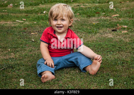 Sorridente giovane ragazzo seduto sull'erba Foto Stock