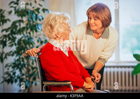 Giovane donna alla conversazione di chiudere un senior che siede in una sedia a rotelle Foto Stock