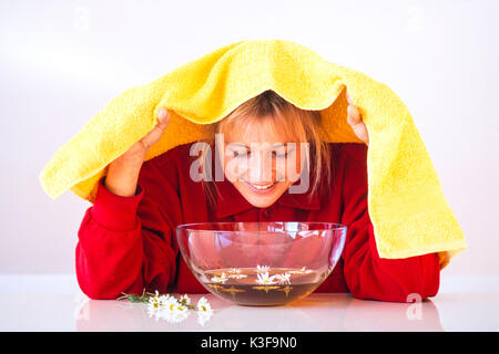 Donna mentre inalazione su un bagno di vapore vicino fiori di camomilla Foto Stock