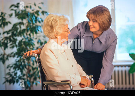 Giovane donna alla conversazione di chiudere un senior che siede in una sedia a rotelle Foto Stock