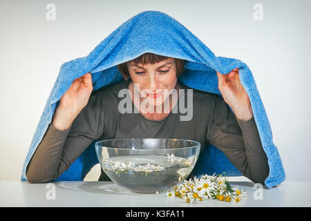 Donna mentre inalazione su un bagno di vapore vicino fiori di camomilla Foto Stock