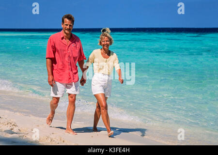 Una coppia passa per una passeggiata mano nella mano in spiaggia Foto Stock