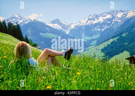 Giovane donna risiede nel prato di fronte panorama di montagna, Alpbachtal, Tirolo Foto Stock
