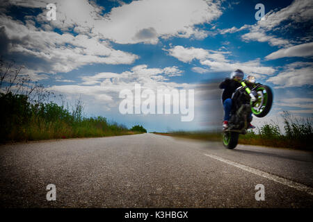 Riding motociclo su una ruota sulla strada vuota e clowdy cielo blu Foto Stock