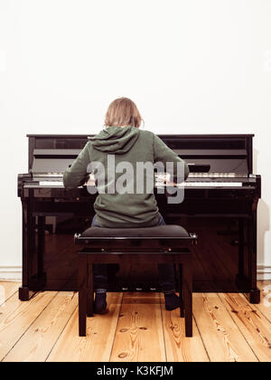 Vista posteriore di un ragazzo giocando su un nero pianoforte digitale Foto Stock