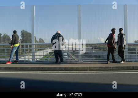 I rifugiati guarda il traffico sulla strada di avvicinamento da un ponte dietro una recinzione alta. I rifugiati sono tornati a Calais, quasi un anno dopo il campo profughi noto come la giungla è stata smantellata dallo Stato francese e i rifugiati sono stati inviati ai centri di accoglienza in tutta la Francia. I rifugiati stanno ancora cercando di raggiungere il Regno Unito. In un modo che stanno cercando di inserire i carrelli lungo il percorso 216 Nazionale, la strada che conduce al porto di Calais e la Ferries andando per il Regno Unito, quando il traffico è fermo sulla strada. (Foto di Michael Debets/Pacific Stampa) Foto Stock
