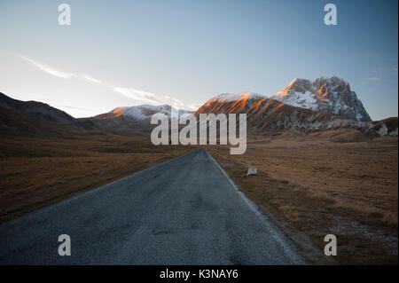 Una strada nel Campo Imperatore altopiano con il Corno Grande del Gran Sasso d'Italia il picco sullo sfondo, Abruzzo, Italia Foto Stock