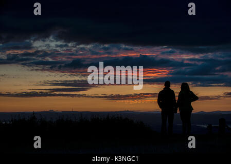 Un giovane tenere mani come guardare il tramonto dal picco Coaley nel Gloucestershire. Foto Stock