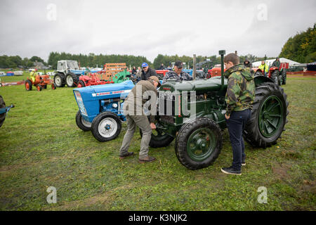 Un uomo usa un manico per avviare il suo trattore d'epoca mentre gli appassionati di trattori e vapore sfilano sotto la pioggia al Northleach Steam & Vintage show, Gloucestershire. Foto Stock