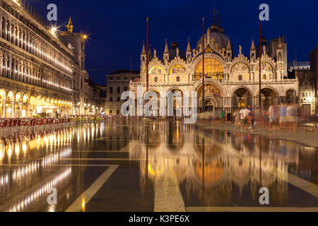 Basilica di San Marco illuminata di notte durante le ore di colore blu riflessa nell'acqua ancora di acqua alta in Piazza San Marco, Venezia , Veneto, Italia con Foto Stock