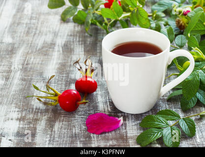 Tè da una rosa canina in una tazza alta su un sfondo di legno con frutti. Foto Stock