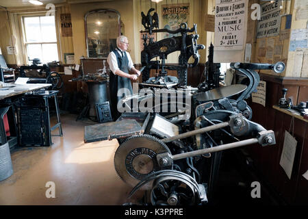 Anziani, maschi di lavoro della stampante flatbed vintage stampa circondato da vintage incudine di stampa premere Foto Stock