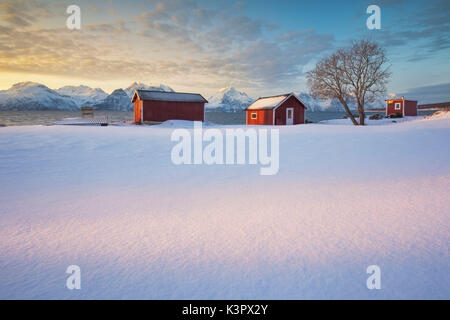 Il cielo arancione al tramonto il telaio il mare ghiacciato e tipici Rorbu immerso nella neve Djupvik Alpi Lyngen Tromsø Norvegia Europa Foto Stock