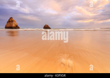 Cielo rosa al tramonto su rocce e spiaggia di sabbia circondate dal mare limpido Praia dos Tres Irmaos Portimao Algarve Portogallo Europa Foto Stock