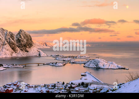 Il colore rosa del tramonto e vette innevate circondano i villaggi di pescatori Reine Nordland Isole Lofoten in Norvegia Europa Foto Stock