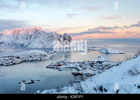 Il colore rosa del tramonto e vette innevate circondano i villaggi di pescatori Reine Nordland Isole Lofoten in Norvegia Europa Foto Stock