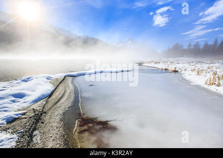 Inverno il sole illumina il lago ghiacciato di Silvaplana circondato da nebbia Maloja Cantone dei Grigioni Engadina Svizzera Europa Foto Stock