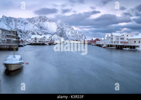 Il tipico villaggio di pescatori di Henningsvaer circondato da montagne innevate e il freddo mare Isole Lofoten Norvegia del Nord Europa Foto Stock