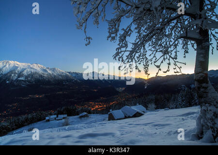 Luci del tramonto illuminano la valle e la coperta di neve di capanne tagliate di sopra di Gerola Alta Valtellina Lombardia Italia Europa Foto Stock