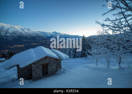 Luci del tramonto illuminano la valle e la coperta di neve di capanne tagliate di sopra di Gerola Alta Valtellina Lombardia Italia Europa Foto Stock