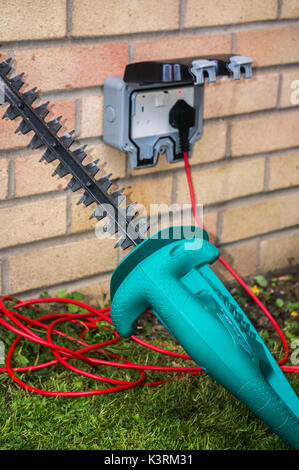 Tagliasiepi inserito in un esterno di alimentazione su una casa residenziale parete. Tre pin, British, doppie prese elettriche, Inghilterra, Regno Unito. Foto Stock