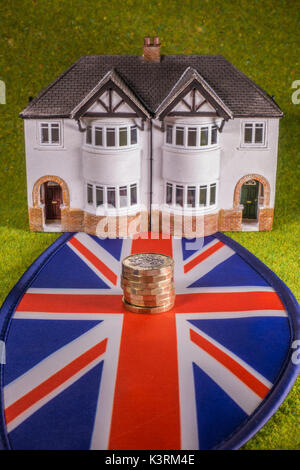 Modello di casa, Sterling Pound monete (con nuovo £ 1 moneta) e Union Jack, per raffigurare costa come un regno unito aumento dei tassi, home comprare, affittare, spostamento, ecc. Foto Stock