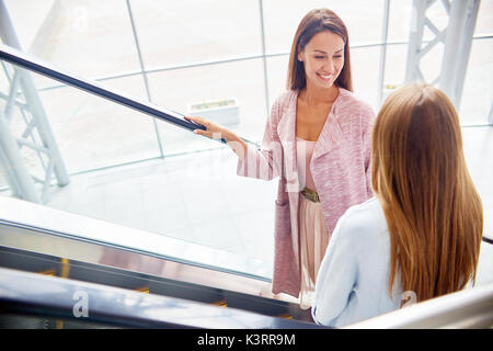 Elevato angolo di due giovani donne su scala mobile nel centro commerciale per lo shopping, per chattare e sorridente felicemente mentre andando fino Foto Stock